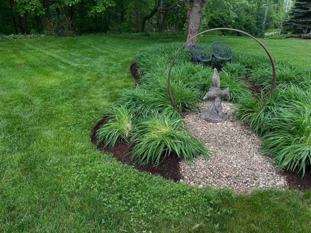 Mulched garden bed with ornamental grasses and shrubs along the edge of a mowed lawn.