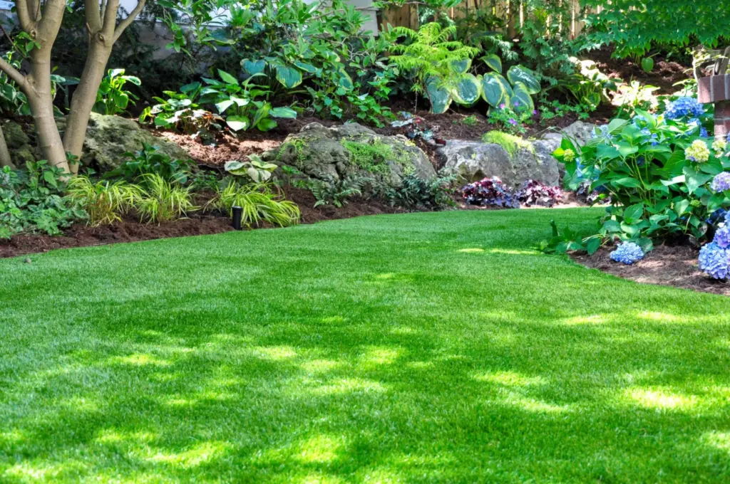 Wide backyard lawn bordered by mature trees and planting beds.
